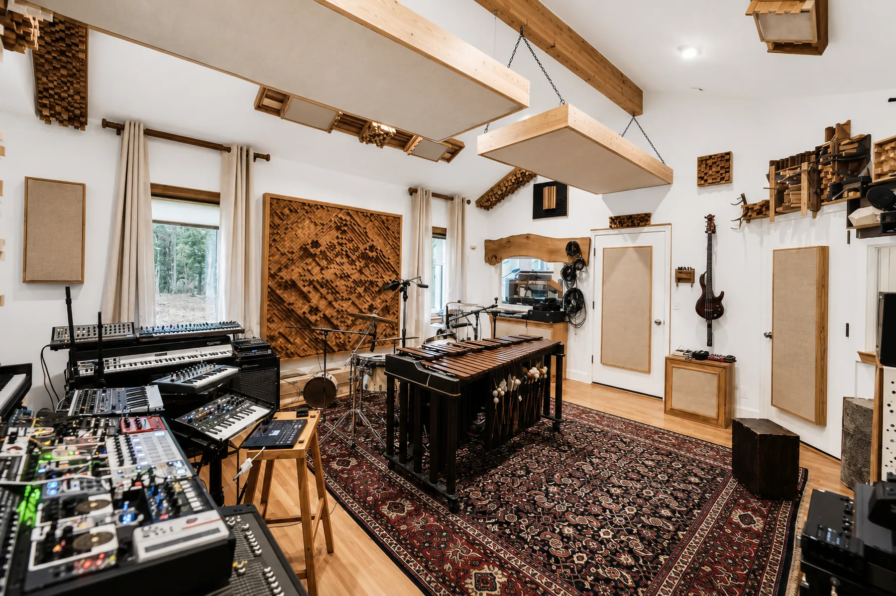 The studio control room seen wide — mixing desk, upright piano and guitars under the beams